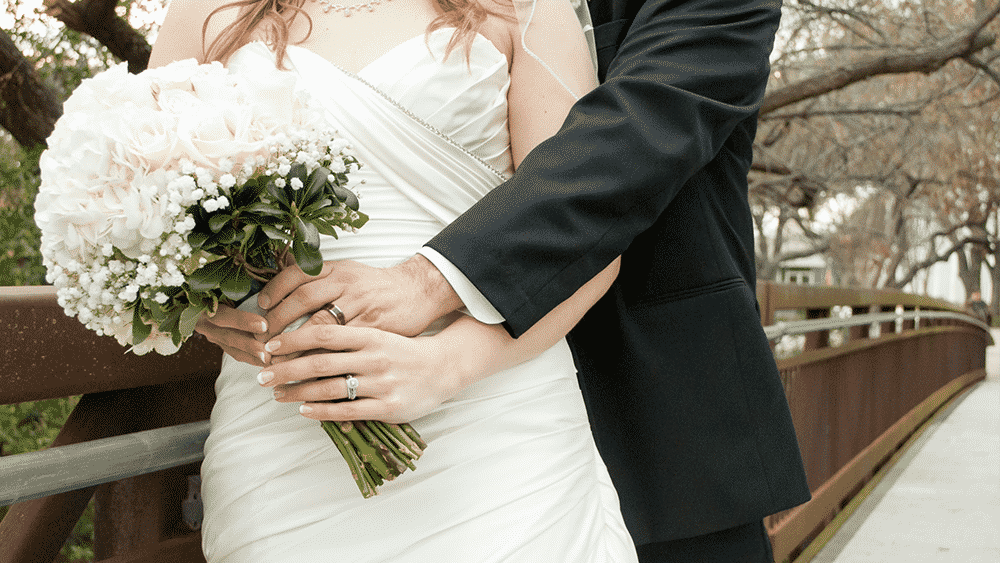 Noivos abraçados durante casamento; para viajar, terão que alterar passaporte após mudança de nome